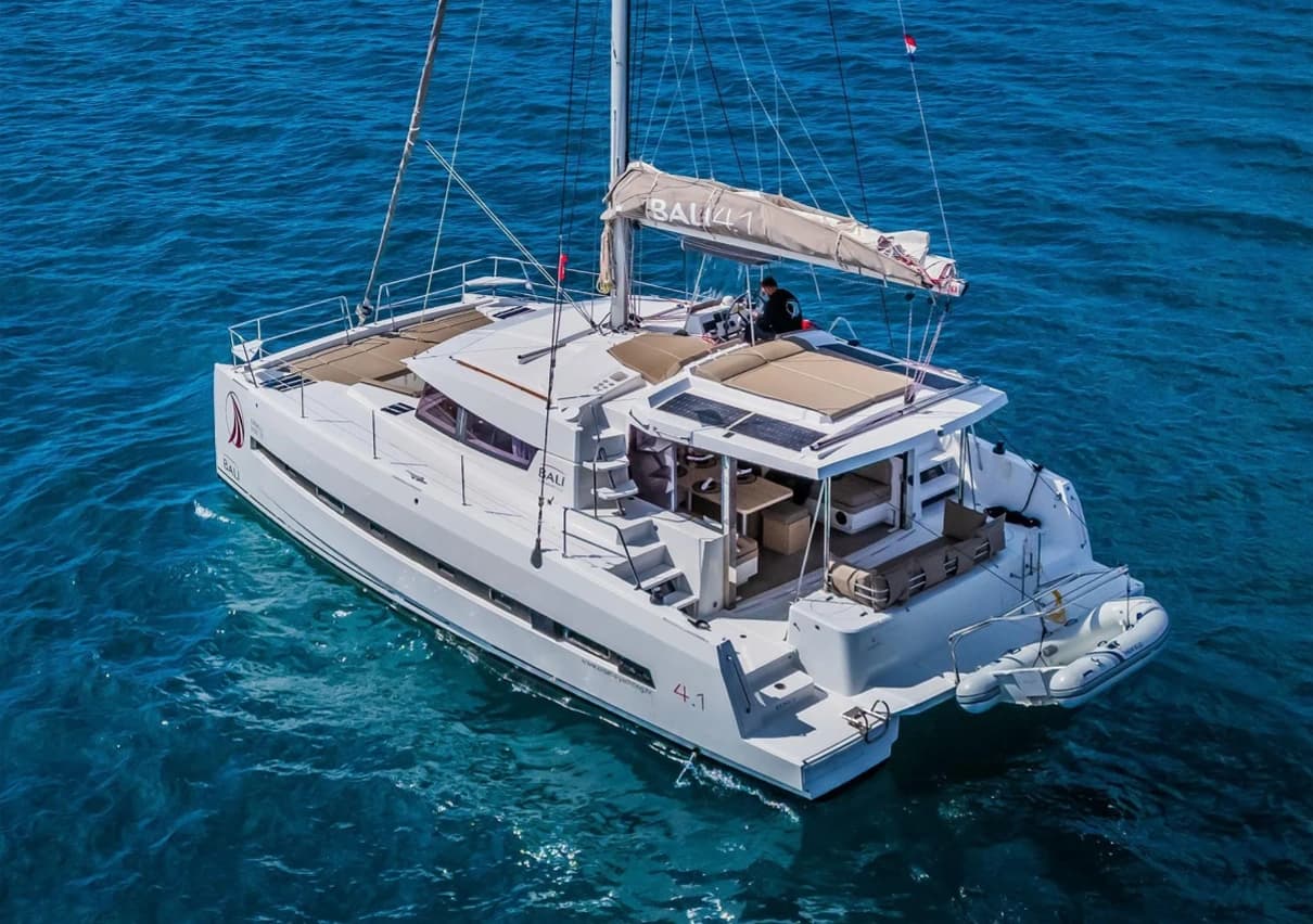 A white sailing catamaran anchored in clear blue water