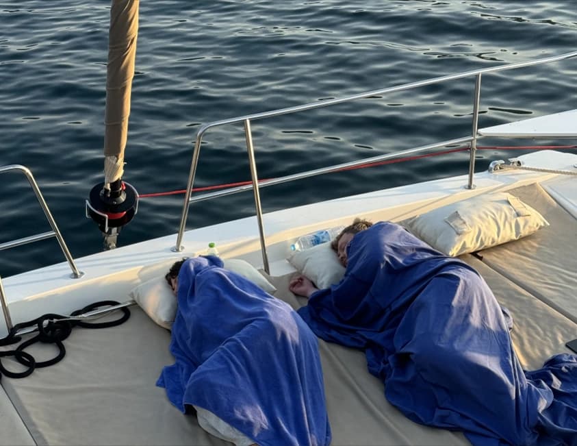 Two people resting under blue blankets on a yacht’s deck